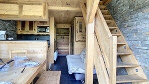 Une petite cabane en bois comprenant un coin cuisine, une table à manger et un espace nuit.