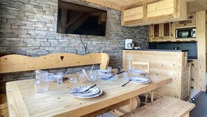 Une table de salle à manger en bois, mise avec des assiettes, des verres et des couverts, un mur en pierre et des meubles en bois, dont un contenant un four à micro-ondes.