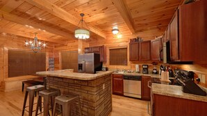 A kitchen with wooden cabinets, a central island with stools, a refrigerator, a dishwasher, and a coffee maker.