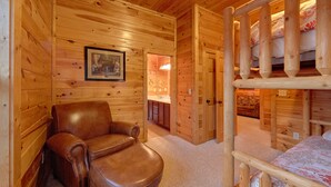 A wooden cabin interior with a leather armchair, a bunk bed, and a framed picture on the wall.