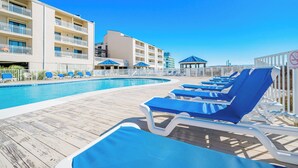 A poolside area with blue lounge chairs, a wooden deck, and a building with balconies. - BEACH VIEW! One Bedroom at Sugar Beach Condos (Orange Beach)