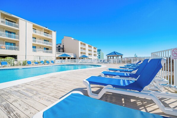 A poolside area with blue lounge chairs, a wooden deck, and a building with balconies.