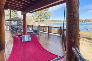 Una terraza de madera con una hamaca, sillas y una mesa, con vista a un cuerpo de agua.