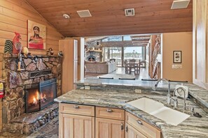 A kitchen with a stone fireplace, wooden cabinets, and a large island with a sink.