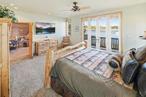 Un dormitorio con una cama grande, cabecera de madera, vista a un lago a través de puertas correderas y un ventilador de techo.