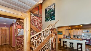 A wooden staircase with a natural design, leading to a kitchen area with a bar and stools. - Destro's Lakefront by Destination Big Bear : Luxury Lakefront! HOT TUB! PET FRIENDLY 🐾! Pool Table! WiFi! EV Charger! (Big Bear Lake)