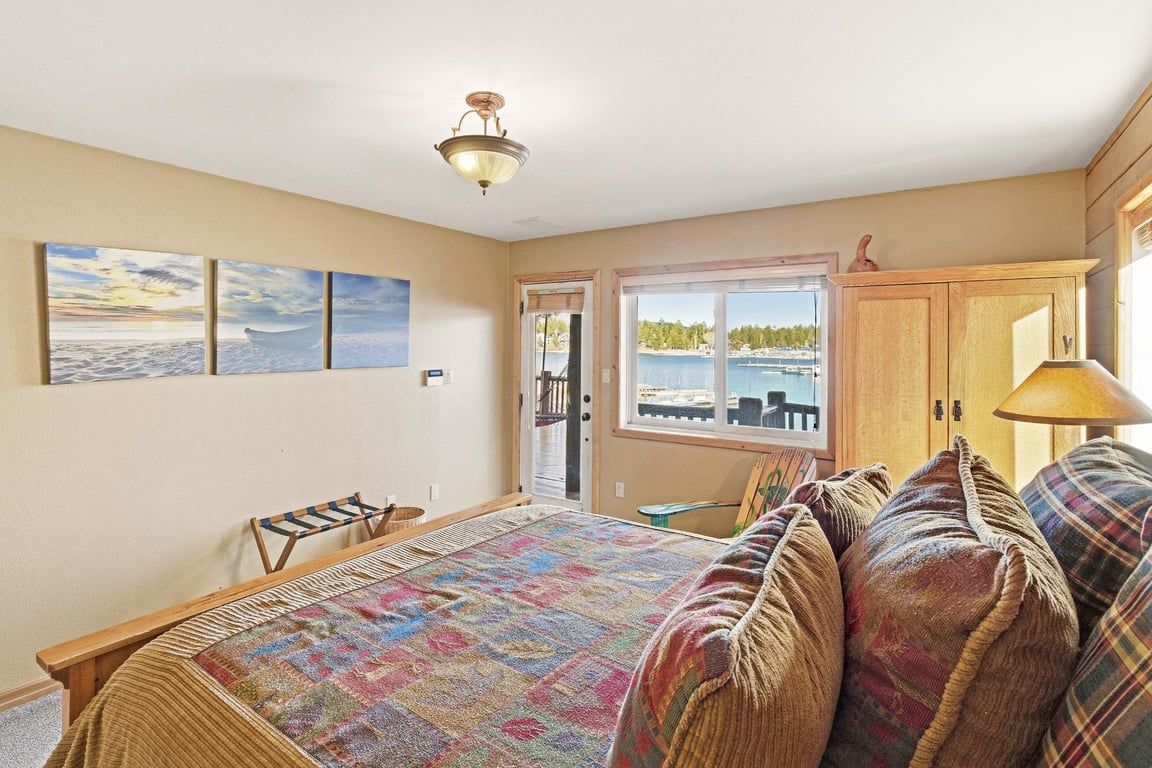 A bedroom with a bed, a window with a view of the water, and a door leading to another room.