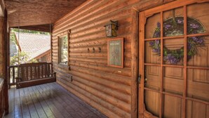 Una cabaña de madera con un porche, un letrero de bienvenida y una puerta adornada con flores moradas.