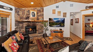 Un interior de cabaña acogedor con chimenea de piedra, sofá de cuero y un televisor grande.