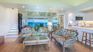 Amplia sala de estar con balcón con vistas al mar, cocina equipada con electrodomésticos modernos y escalera que conduce a un nivel superior.