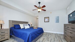 A bedroom with a bed, wooden headboard, nightstands, a dresser, a ceiling fan, and a television.