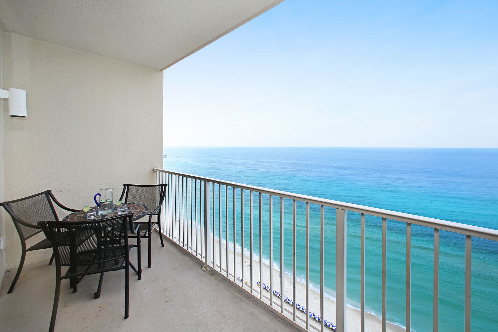 Ein Balkon mit Tisch und Stühlen, der auf einen Strand mit freiem Blick auf das Meer blickt.