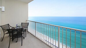 A balcony with a table and chairs, overlooking a beach with a clear view of the ocean.