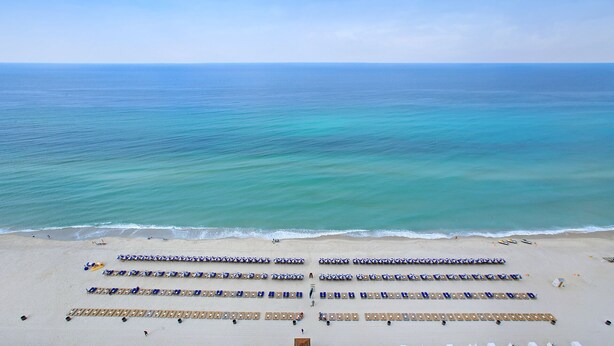 A beach with rows of sun loungers and umbrellas, a clear view of the ocean, and a sandy beach.