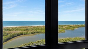 Blick durch ein Fenster auf eine Küstenlandschaft mit Wasserflächen und Vegetation.