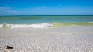 Ein Strand mit klarem, blauem Wasser, ein Boot in der Ferne und ein Kiesufer.
