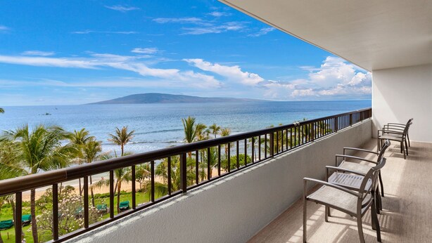 Un balcon avec vue sur l’océan et une montagne. On y trouve des chaises et une table.