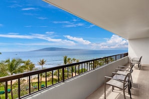 Een balkon met uitzicht op de oceaan en een berg. Er staan stoelen en een tafel op het balkon.