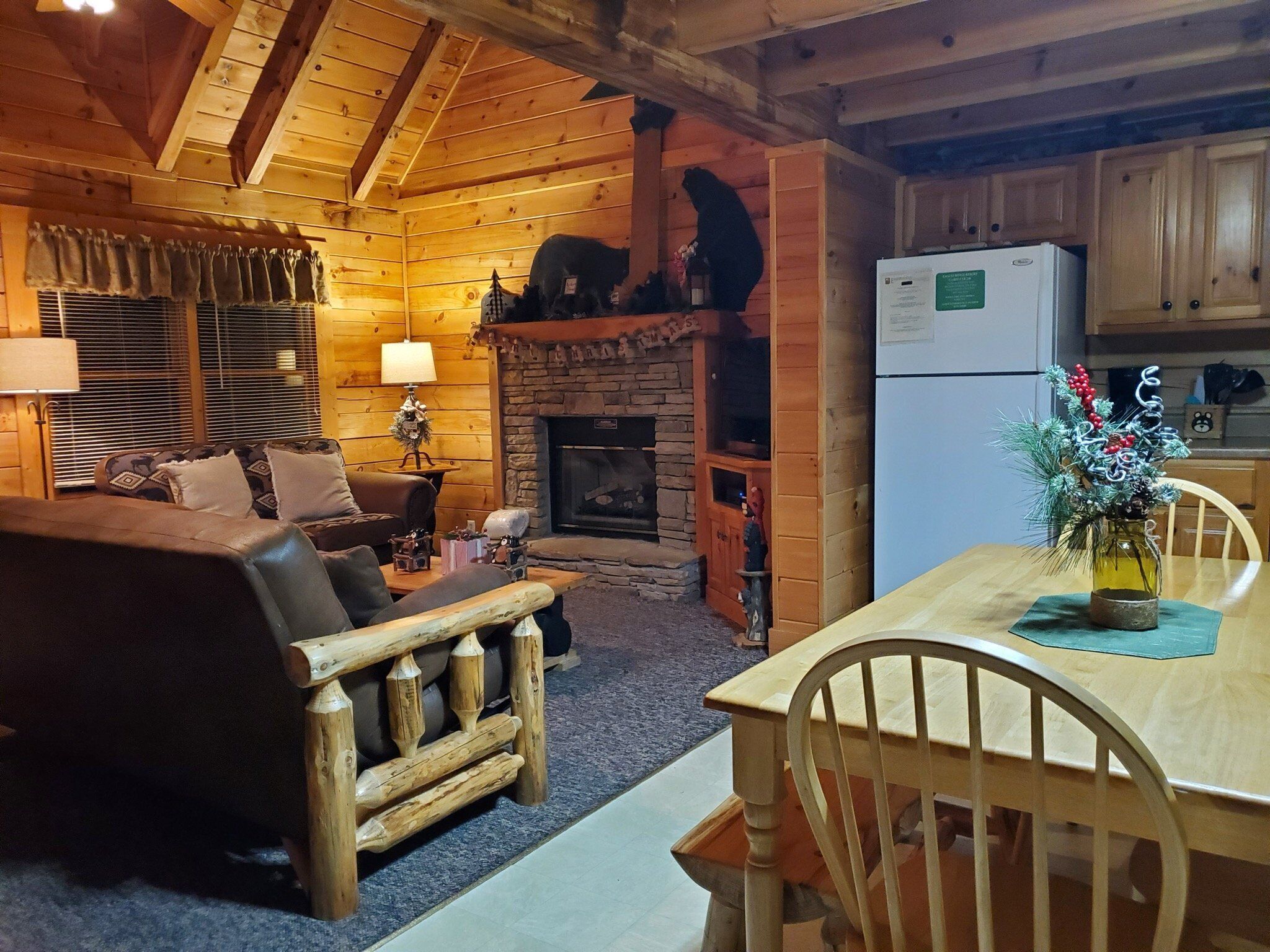 A cozy log cabin interior with a living room, fireplace, dining area, and kitchen.