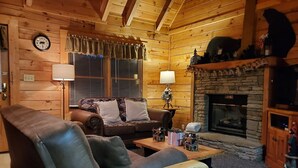 A cozy log cabin interior with a leather sofa, a wooden coffee table, a fireplace, and a clock on the wall. - ER 246 – The Getaway  Great Location – Close to town! (Pigeon Forge)