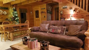 A cozy cabin interior with a wooden dining table, a brown leather couch, and a Christmas tree. - ER 246 – The Getaway  Great Location – Close to town! (Pigeon Forge)