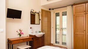 A bedroom with a bed, a wooden desk with a chair, a vanity with a mirror, and a television mounted on the wall.