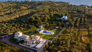 An aerial view of a large estate with multiple buildings, a swimming pool, and a view of the sea.