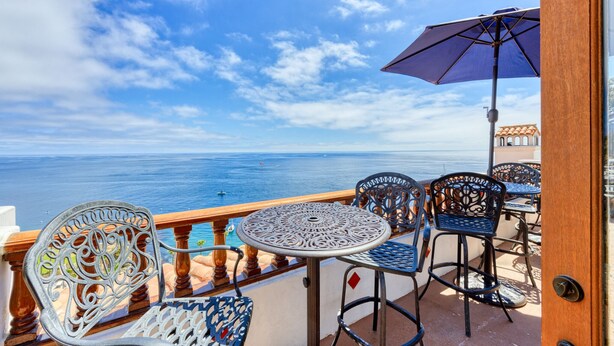 Ein Balkon mit Meerblick, ausgestattet mit verzierten Metallstühlen und einem Tisch.