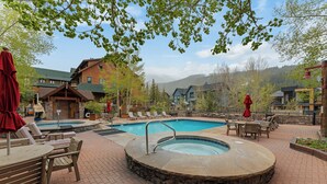 A pool area with lounge chairs and a hot tub, surrounded by buildings and trees. - Penthouse Condo in River Run Village with Slope Views & Short Walk to Gondola (Keystone)