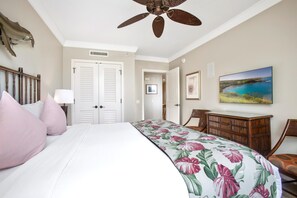 Habitación de hotel con cama, escritorio, silla, ventilador de techo y un cuadro en la pared.