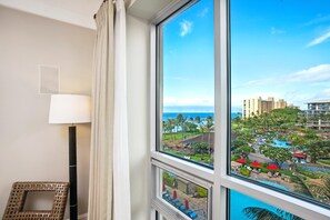 A hotel room with a large window offering a view of a resort with multiple buildings, a pool, and palm trees.