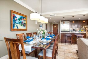 Uma sala de jantar com uma mesa comprida posta para seis, cadeiras de madeira e um quadro na parede.
