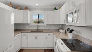 A modern kitchen with white cabinetry, a granite countertop, a built-in stove, and a window with blinds. - Seawinds 1 Beach Front Townhome (Miramar)