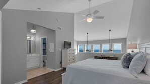 A bedroom with a large bed, a ceiling fan, and a view of the ocean through the windows. - Seawinds 1 Beach Front Townhome (Miramar)