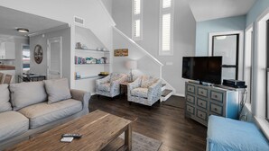 A spacious living room with a high ceiling, a staircase, a television, and a bookshelf. - Seawinds 1 Beach Front Townhome (Miramar)