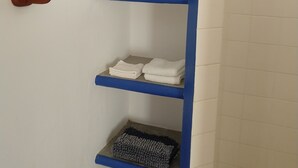 A bathroom with a blue towel rack holding folded towels, a wooden door with a handle, and a tiled shower area. - Hacienda de Palmas: Room #2 Cupola with one queen size bed (La Ribera)