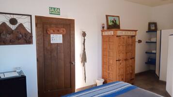 A room with a bed, a wooden wardrobe, a door with an emergency exit sign, and a wall-mounted decoration.