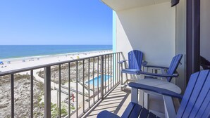 Un balcón con dos sillas azules, una pequeña mesa y vista a la playa y al océano.