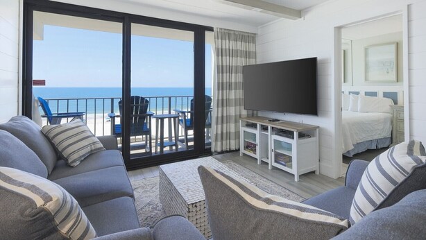 Una habitación con sofá, televisión, cama y balcón con vistas al mar.