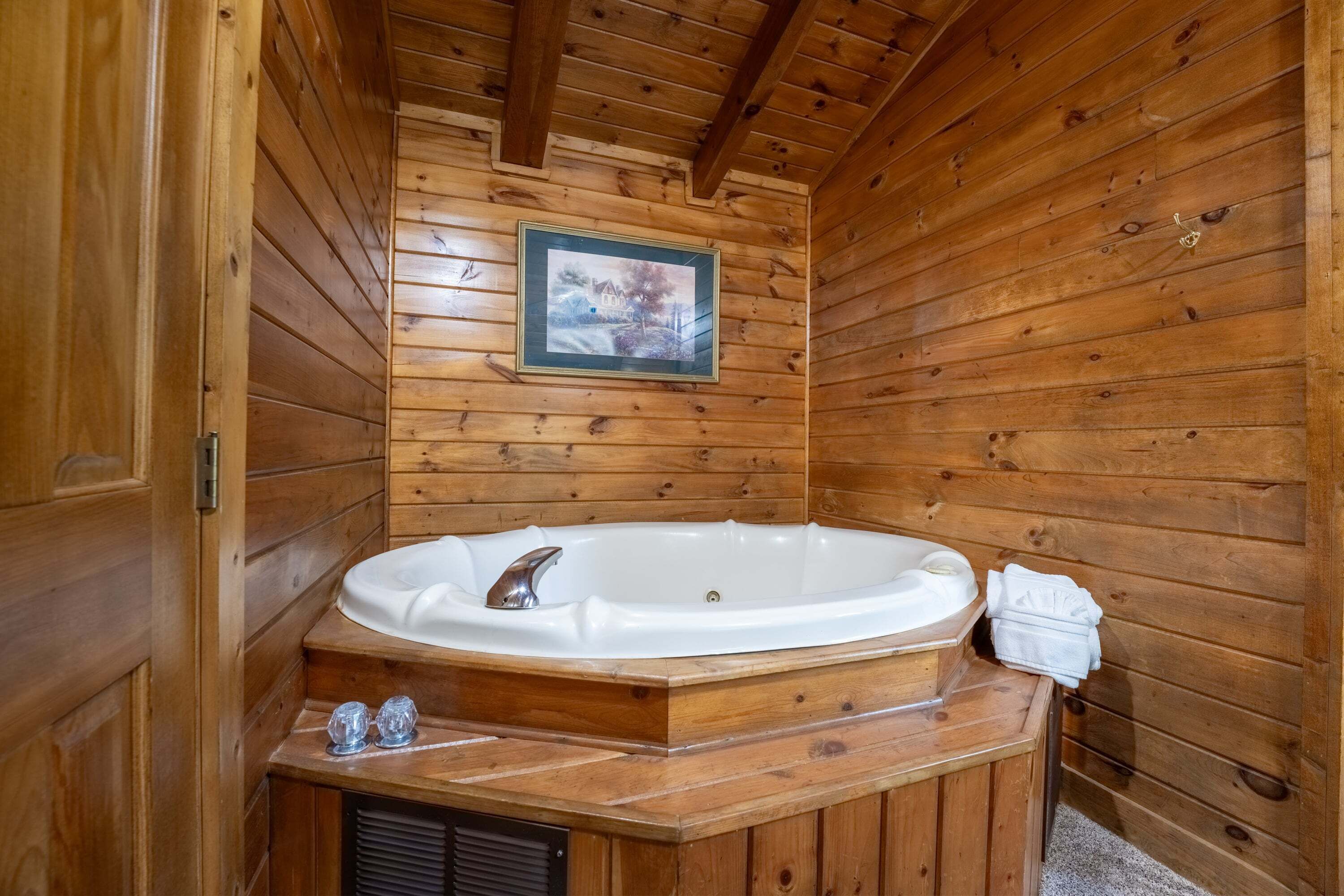 A wooden cabin interior with a wooden bathtub, a framed picture on the wall, and a towel on the side.
