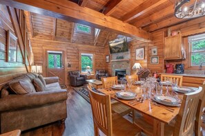 A wooden cabin interior with a dining area, sofa, fireplace, and framed pictures.