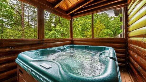 Un jacuzzi en una cabaña de troncos con paredes de madera y ventanas amplias con vistas a un bosque.