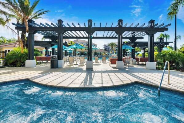 A pool area with a pergola, lounge chairs, and umbrellas.