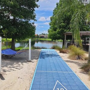 Ein blauer Shuffleboard-Spielfeld mit einer Hängematte und einer Holzhütte in der Nähe eines Sees.