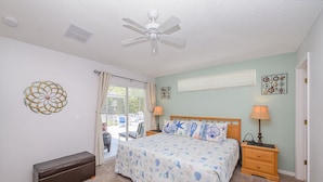 A bedroom with a bed, a bench, a ceiling fan, a window with curtains, and a wall with a decorative piece.