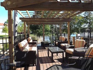 Eine Terrass mit Korbmöbeln, einer Pergola und Blick auf ein Gewässer.