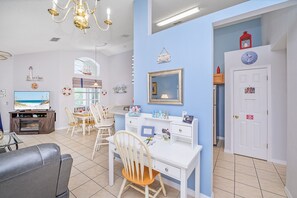 Un salon comprenant un téléviseur, un coin repas et un bureau blanc avec une chaise.