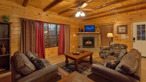 A cozy log cabin interior with a fireplace, leather sofas, a wooden coffee table, and a television. - Serenity Lodge: Theater, Gameroom, Hot Tub (Gatlinburg)