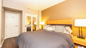 Quarto de hotel com uma cama grande, duas mesas de cabeceira com luminárias, um painel de cabeceira de madeira e uma porta.