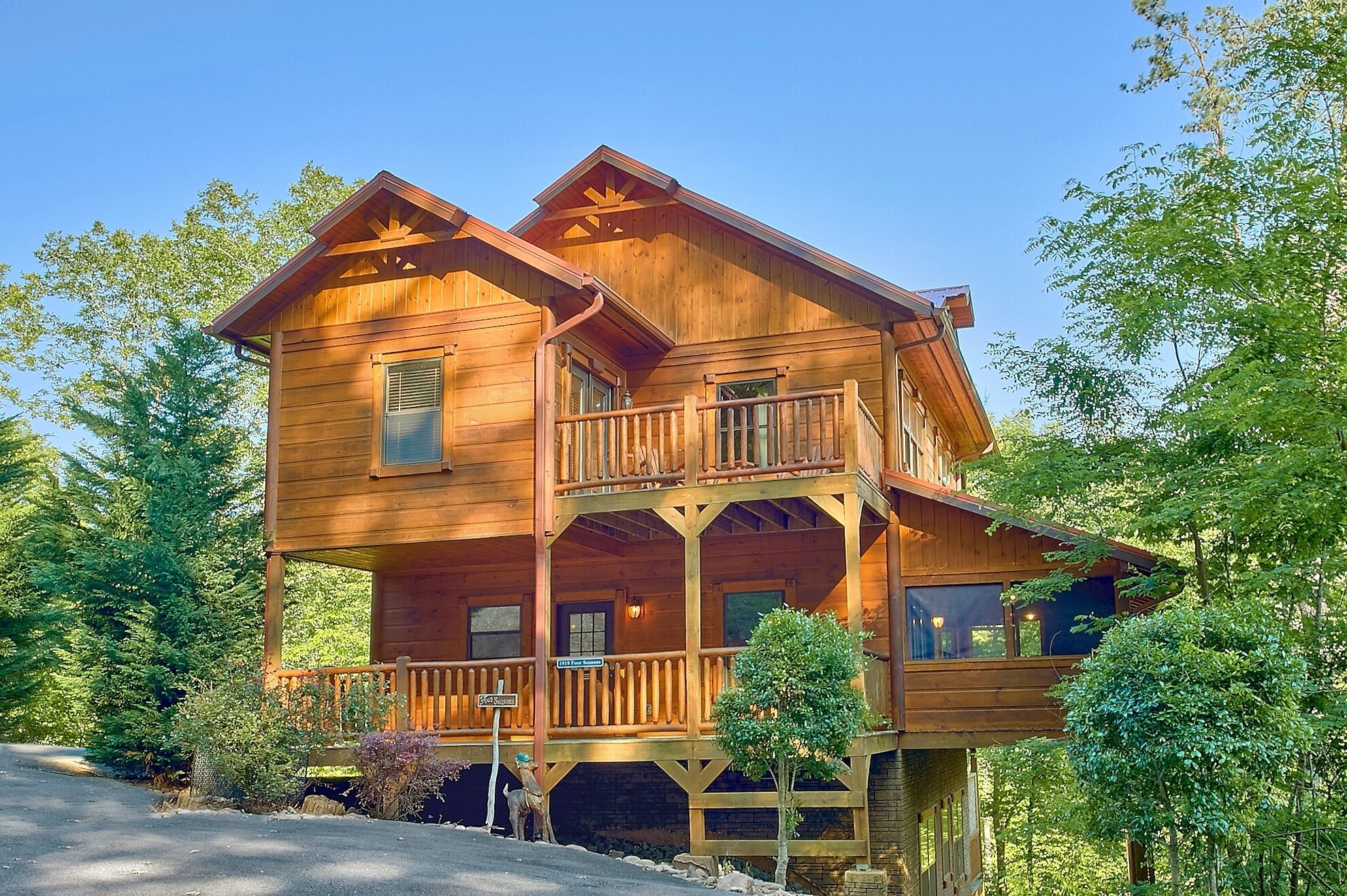 A two-story wooden cabin with a balcony, surrounded by trees.